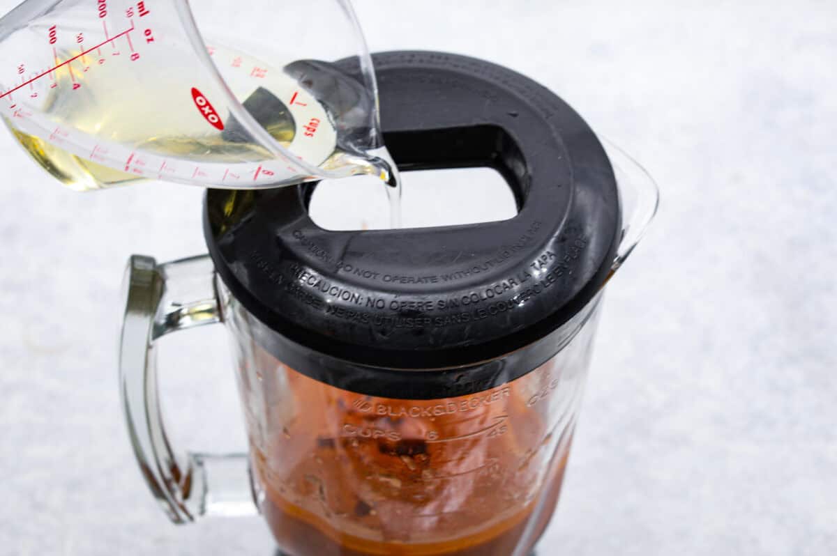 Angle shot of someone pouring oil in a blender with dressing ingredients inside of it. 