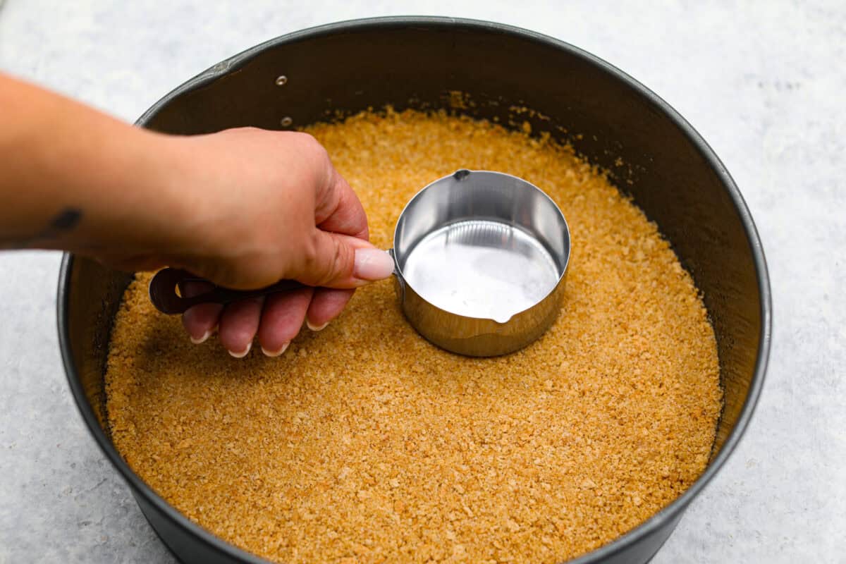 Overhead shot of someone smashing graham cracker crumbs into the springform pan. 