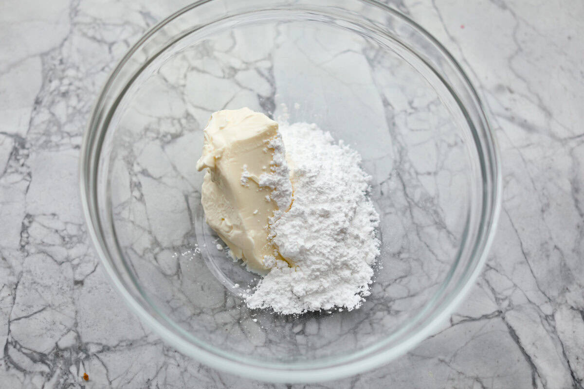 Overhead shot of cream cheese and powdered sugar in glass bowl. 