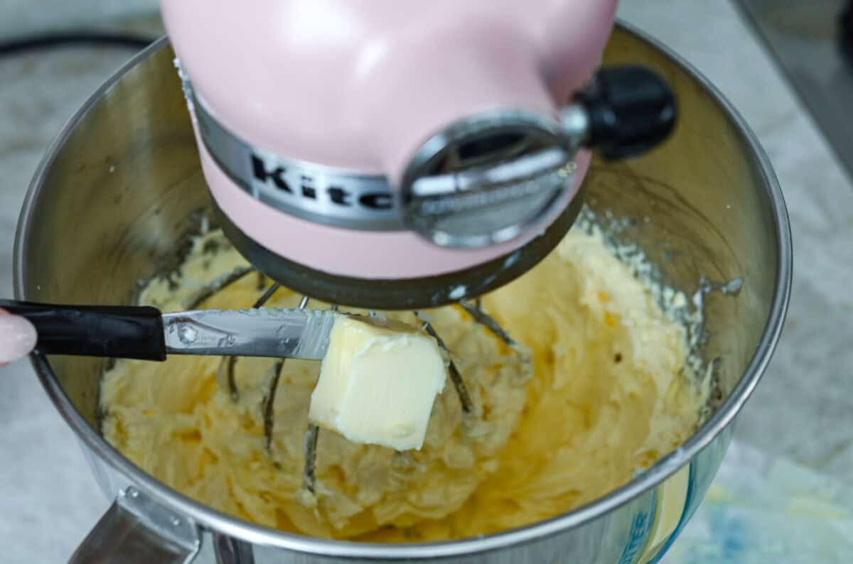 Tablespoon of butter being dropped into a stand mixer that is mixing french buttercream. 