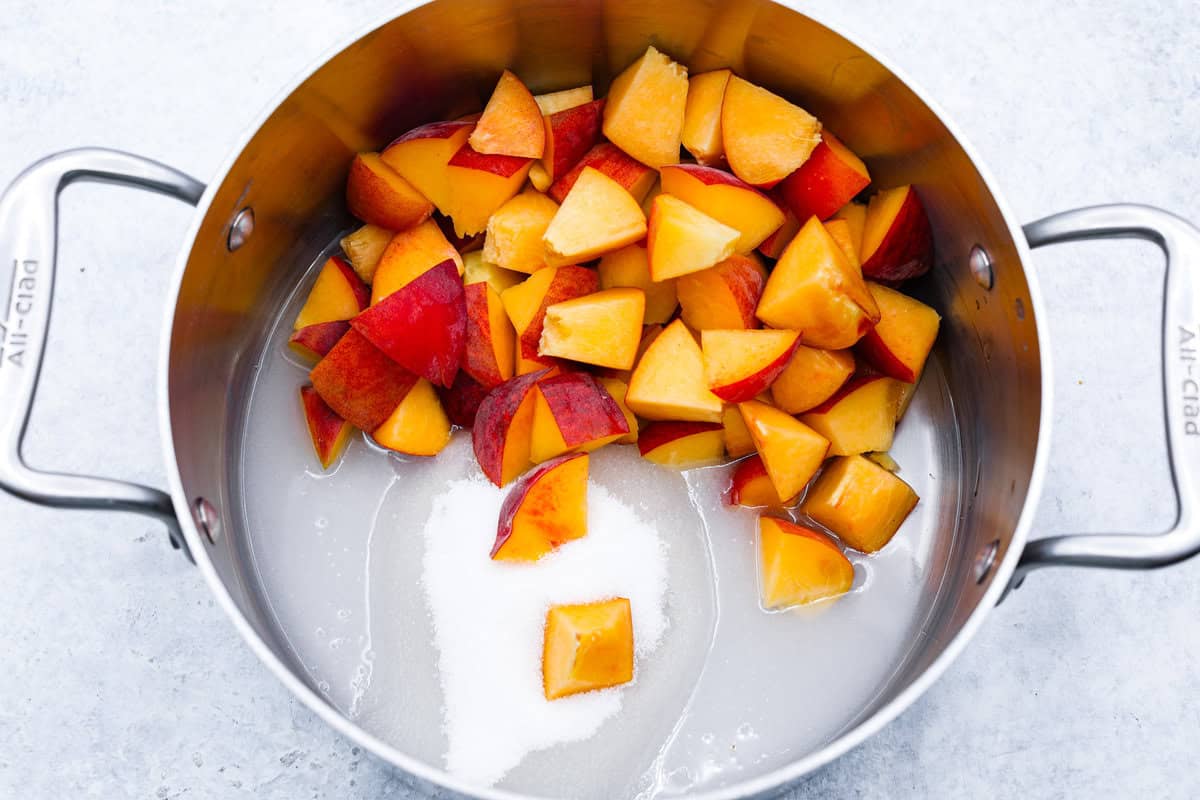This is the absolute BEST fresh peach lemonade recipe! Sweet juicy peaches combined with tart, tangy lemons make the most refreshing drink. You will want to have a pitcher of this in your fridge throughout the peach season! overhead shot of peaches with sugar and water in