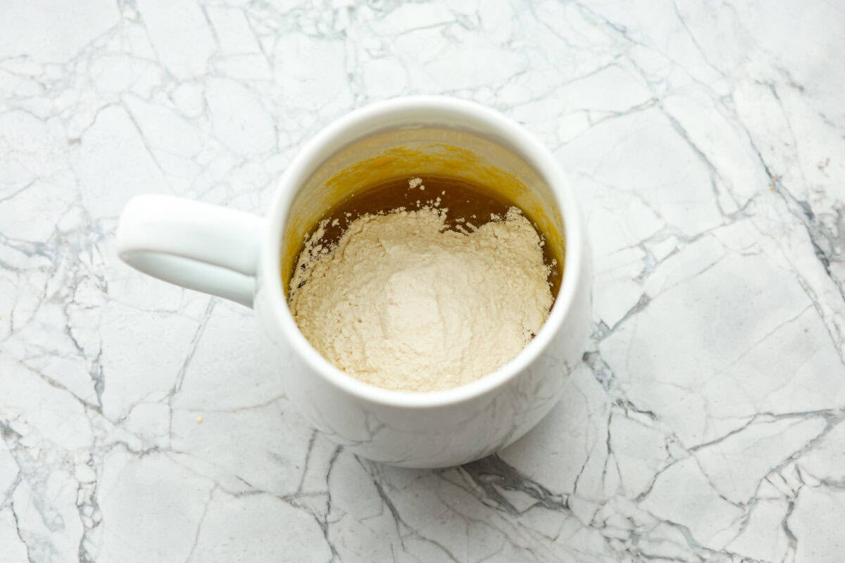 Overhead shot of mug with flour and salt added to sugar, butter and egg mixture. 