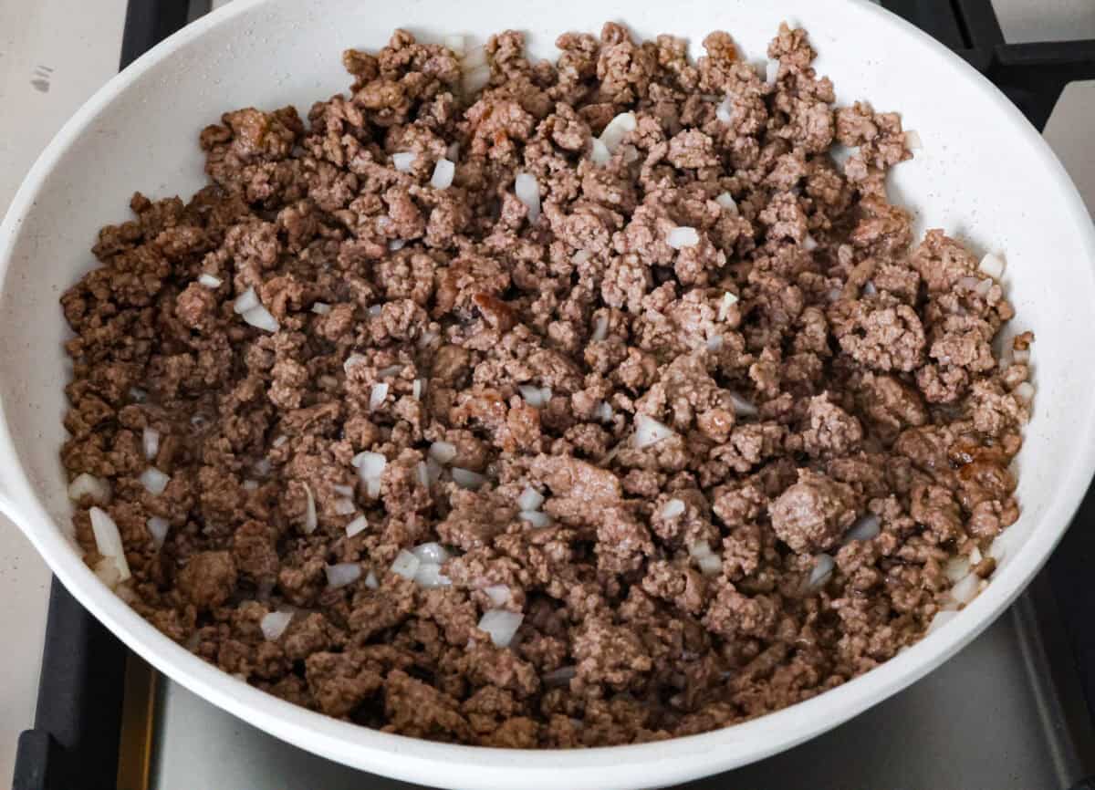 Angle shot of ground beef with onions cooking on the stove top in a skillet. 