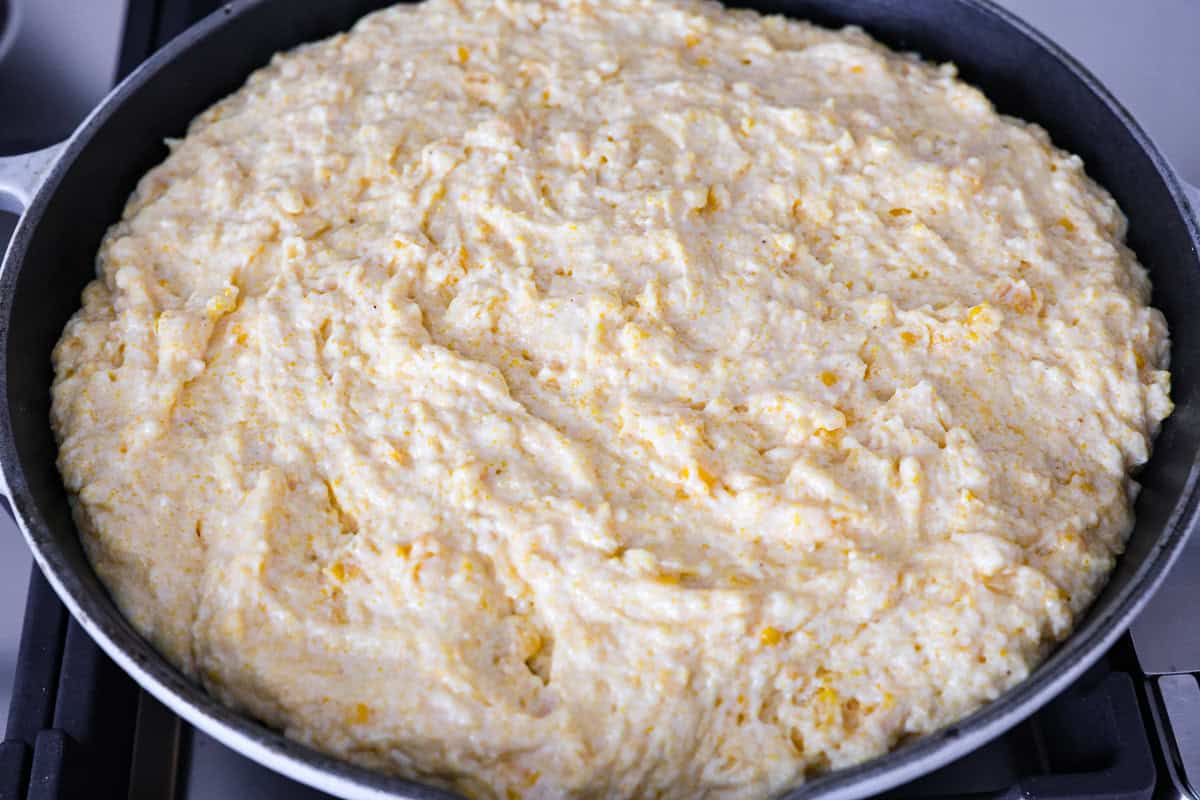 Cowboy Cornbread Casserole is a flavorful, comforting meal that's so easy to make. Seasoned ground beef, corn, pinto beans, and Rotel tomatoes are layered with shredded cheddar cheese and a cornbread topping for a winning dinner! Overhead shot of cornbread batter spread over ground beef and cheese mixture.