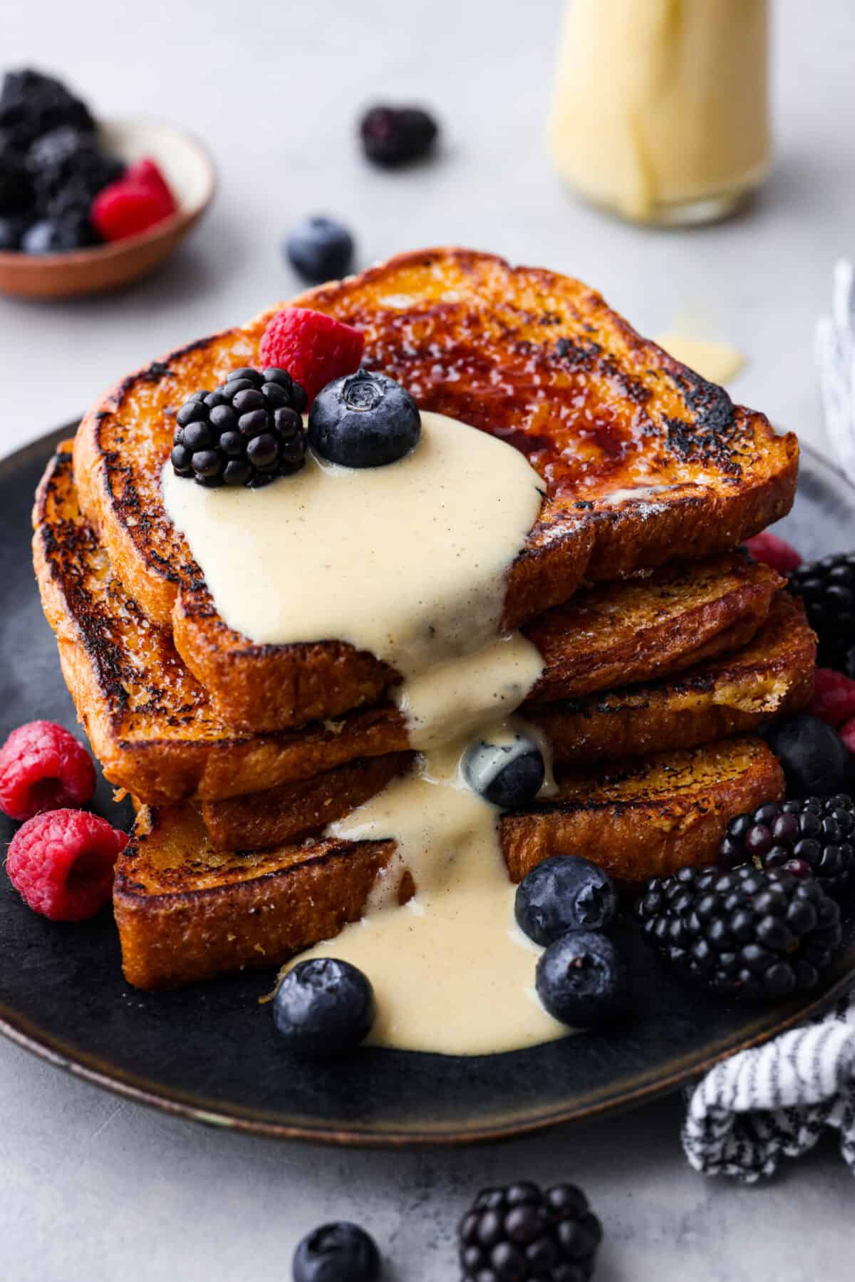 Close view of the stack French toast with creme anglaise sauce and berries on top.