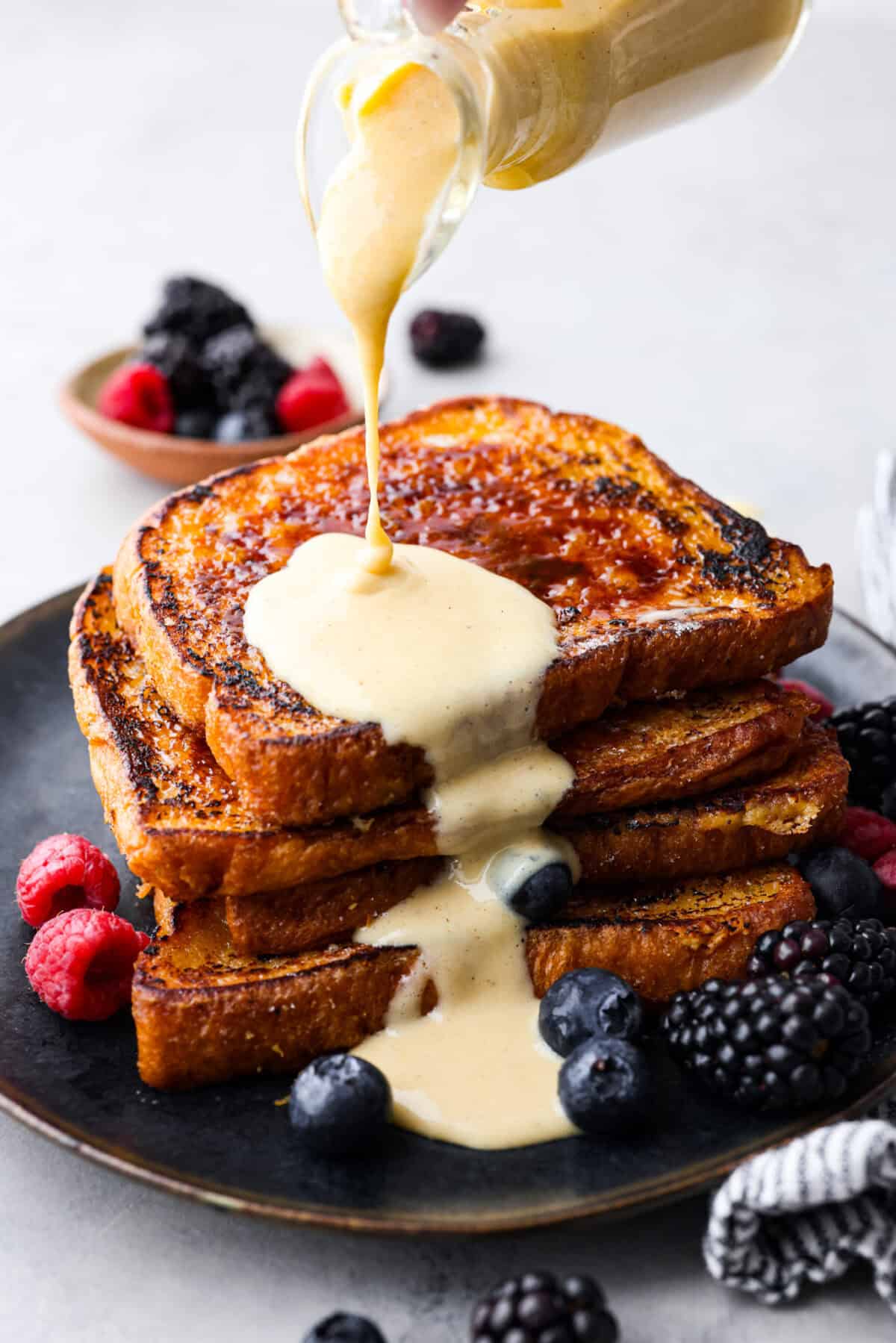 Close view of the creme anglaise sauce pouring on a pile of creme brûlée French toast.