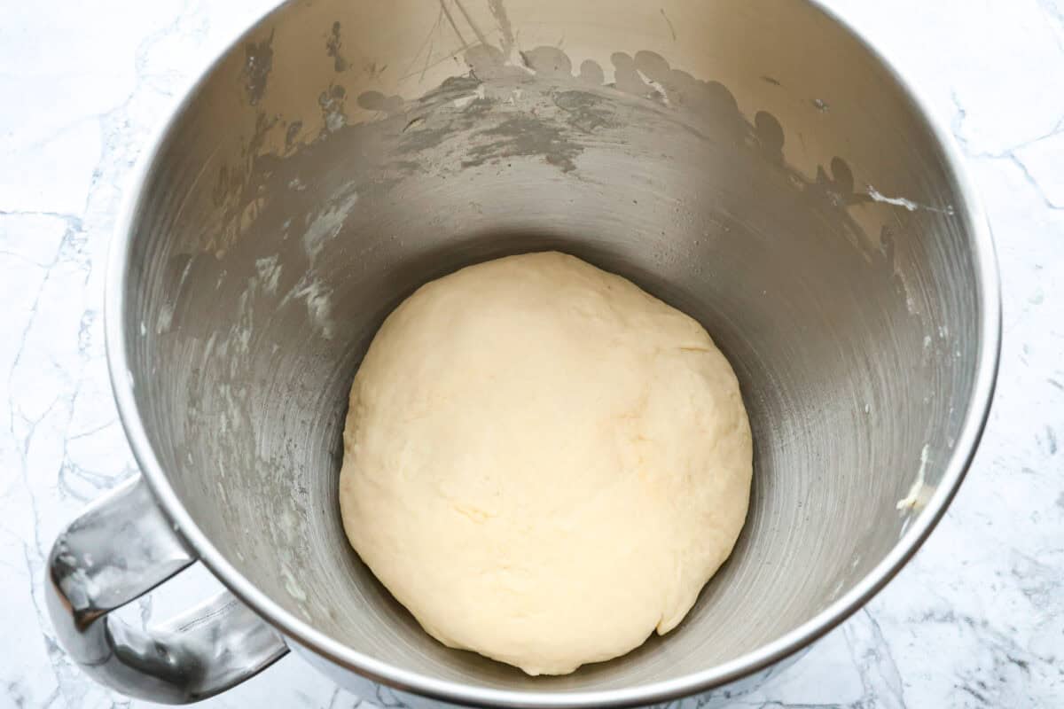 Overhead shot of ball of croissant bread dough at the bottom of stand mixer bowl. 