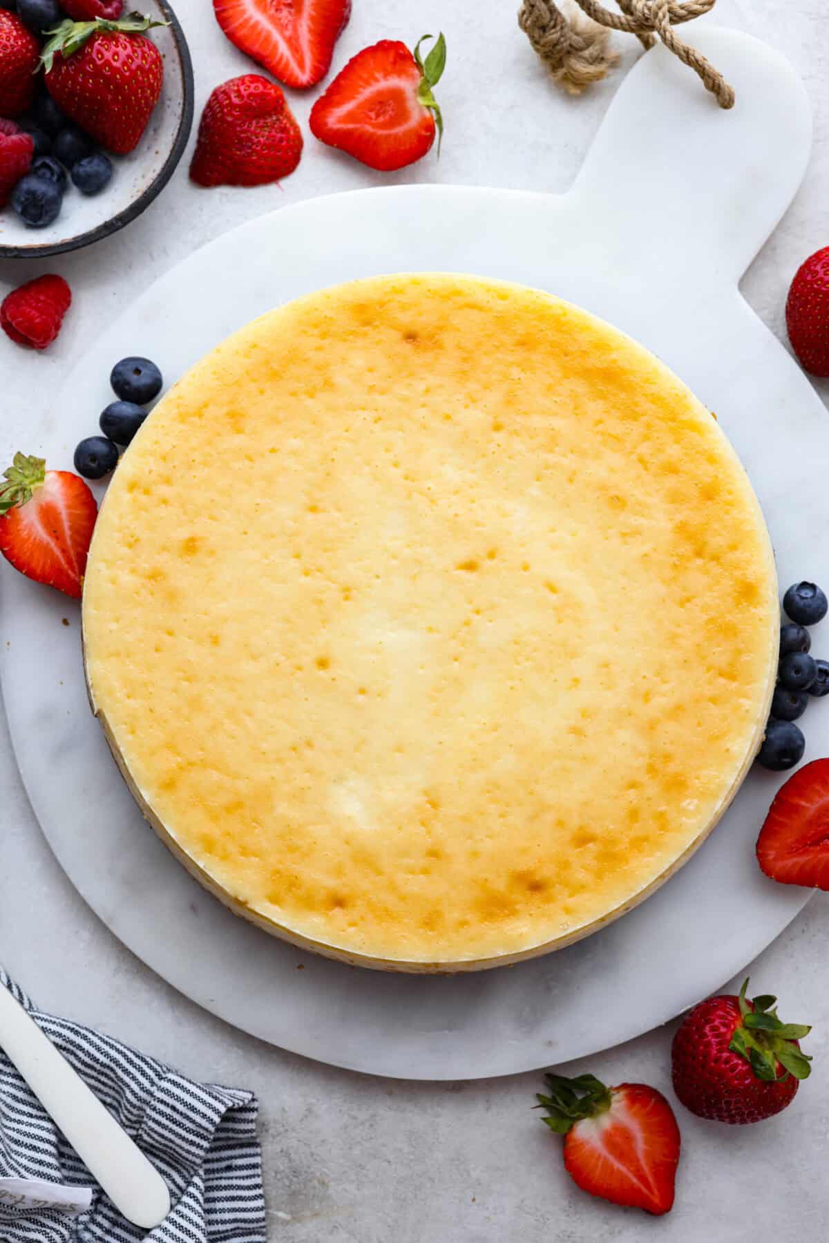 Top view of a whole baked cheesecake with berries on the side.