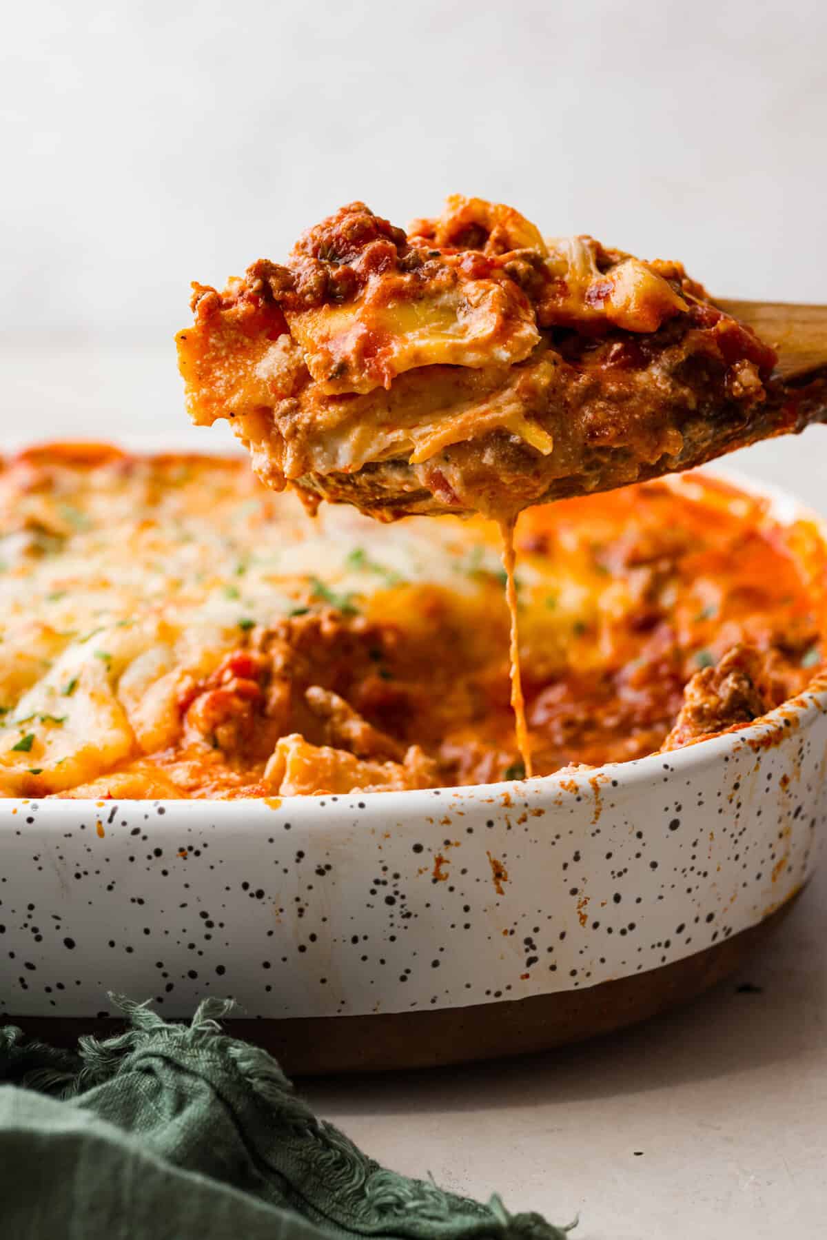 Million Dollar Ravioli Casserole is a flavorful casserole version of the classic! It's easy to make with mouthwatering layers of cheesy ravioli, meat sauce, and melted mozzarella cheese on top. This is a comforting, family-friendly dinner that you'll be craving on repeat! Side shot of a portion of million dollar ravioli casserole being scooped out of the baking dish.