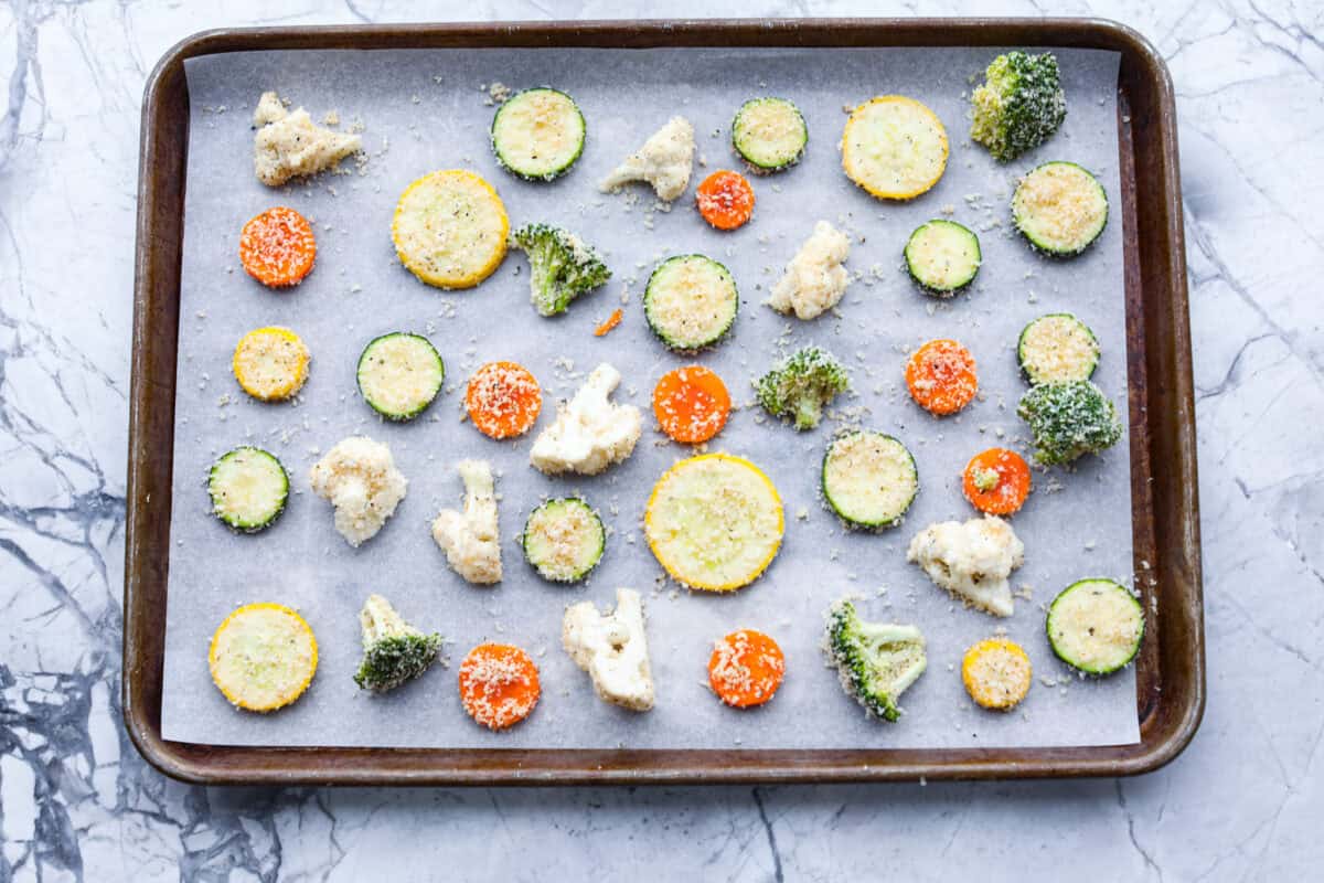 Overhead shot of breaded vegetables spread out on baking sheet.