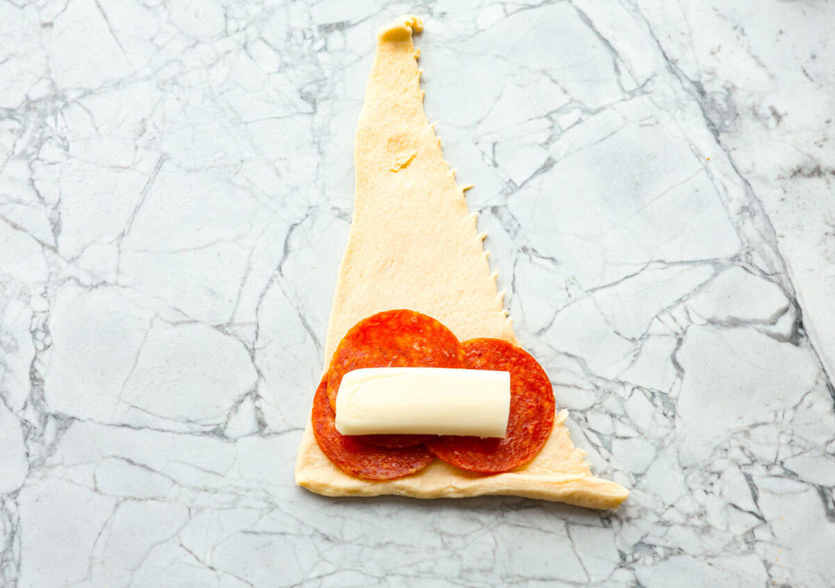 Overhead shot of pepperoni and cheese stick on top of crescent triangle. 