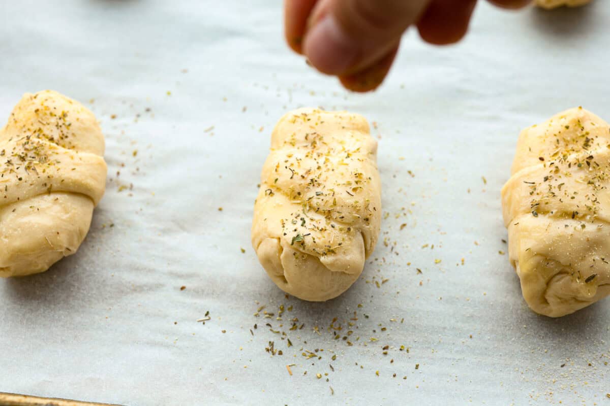 Angle shot of someone sprinkling Italian seasoning on pizza crescent roll. 