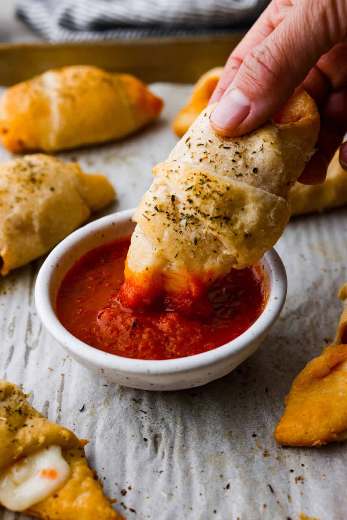 Angle shot of someone dipping a pizza roll into a small bowl of marinara sauce.