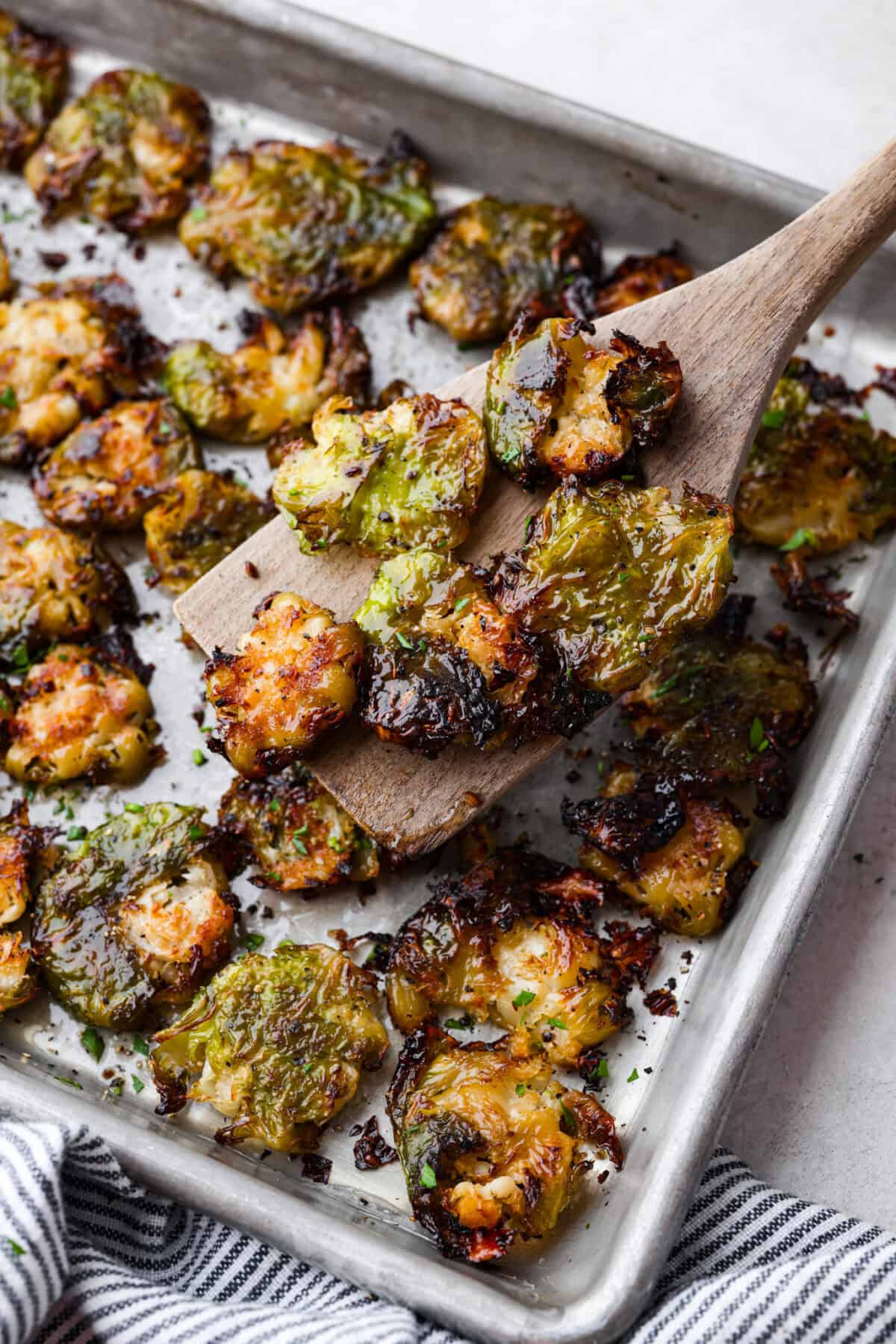 Angle shot of a wooden spatula holding up a few smashed Brussels sprouts out of the pan.