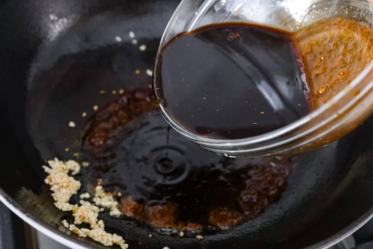 Packed with flavor, these easy Teriyaki Noodles are so much better than takeout! Throw these together in just 20 minutes with pantry staples for the perfect busy weeknight dinner. You can keep it vegetarian or serve it alongside your favorite protein. Overhead shot of someone pouring teriyaki sauce into the skillet with oil and garlic.