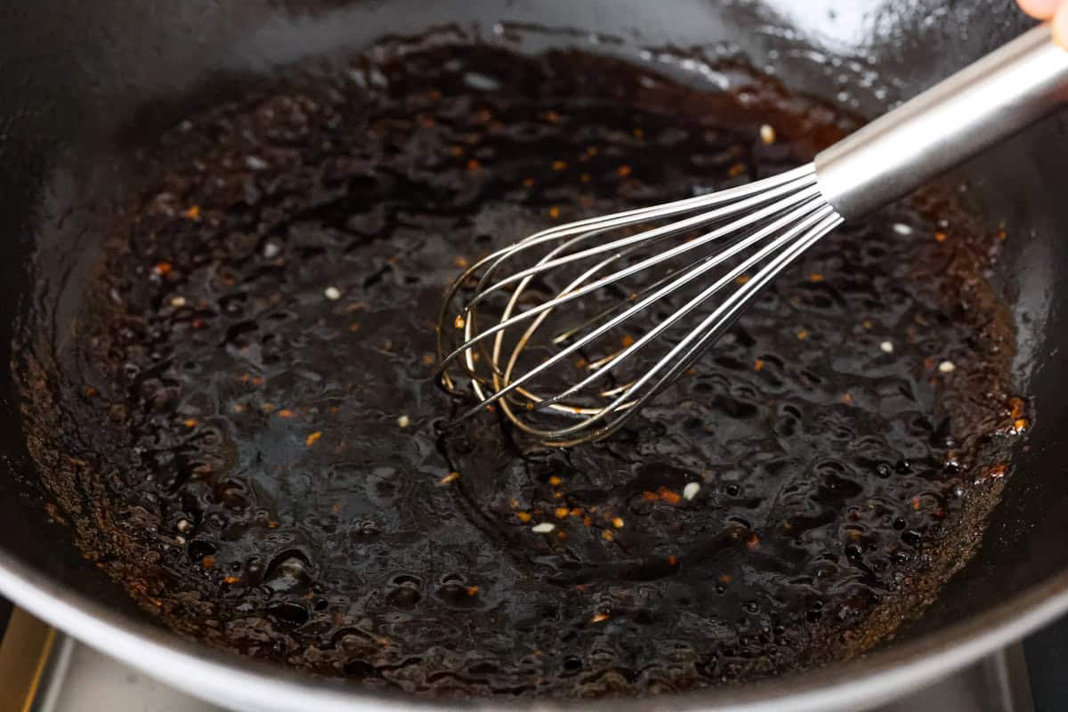 An shot of boiling sauce and oil and garlic in a skillet with someone whisking it.