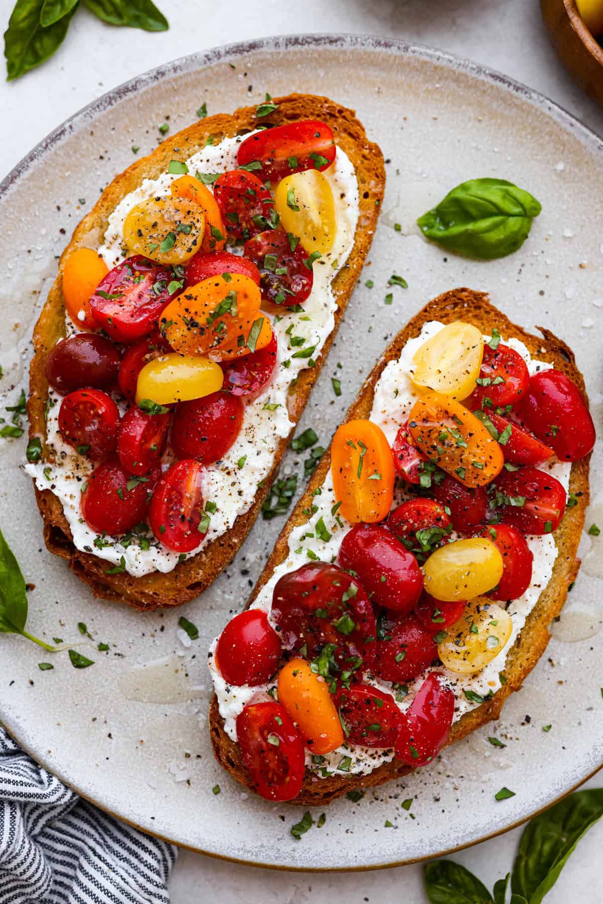 Vibrant Tomato Toast has sweet, juicy tomatoes, garlic, creamy ricotta, and fresh basil layered on a crusty slice of toasted bread. It’s delicious and savory with hints of sweetness. Serve it for breakfast, brunch, as an appetizer, or light lunch for the perfect way to use up summer produce. Overhead shot of plated tomato toast.