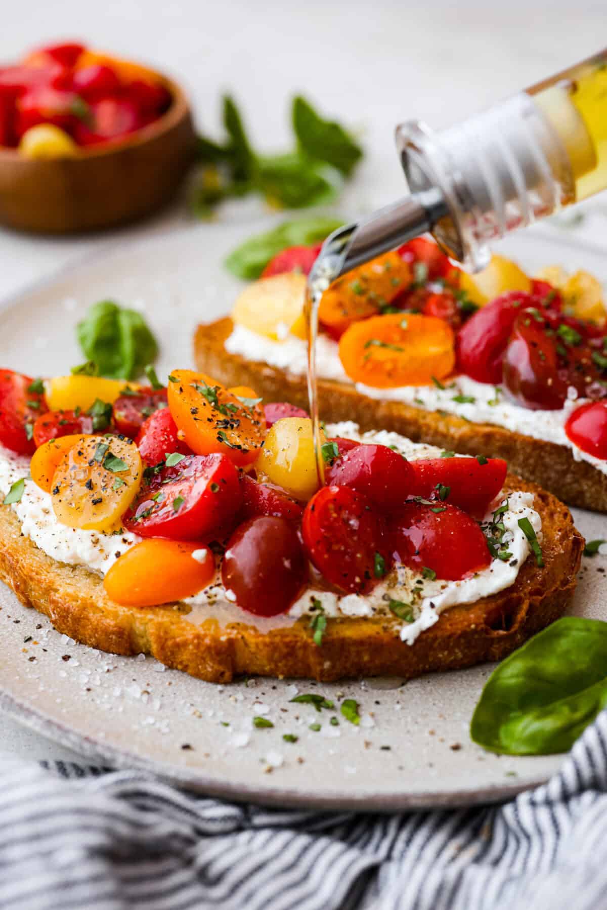 Side shot of someone drizzling olive oil over tomato toast. 