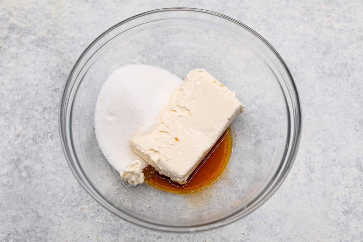 Overhead shot of sugar, cream cheese and vanilla in a glass bowl. 