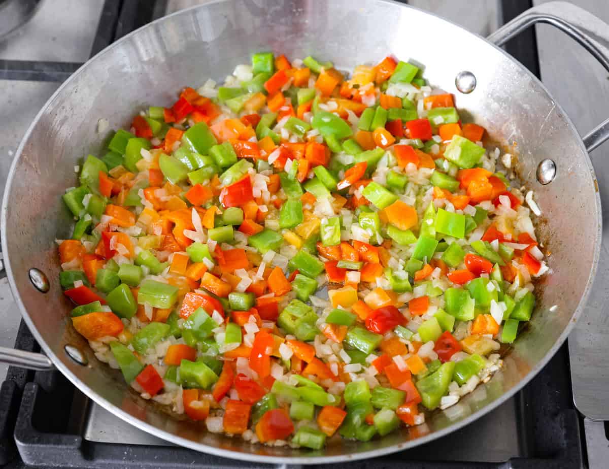 This delicious Louisiana Casserole has become an instant favorite in our house! It has all of the delicious flavors of a jambalaya in an easy-to-make casserole. Tasty andouille sausage, shrimp, veggies, rice and cajun seasoning come together for a complete meal on the table in just 40 minutes! Overhead shot of vegetables being sautéed in butter in a skillet.