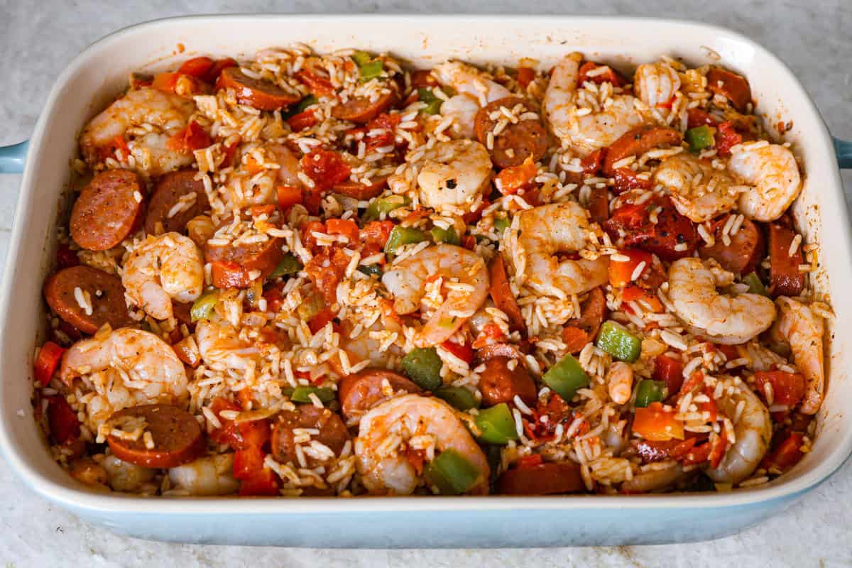 This delicious Louisiana Casserole has become an instant favorite in our house! It has all of the delicious flavors of a jambalaya in an easy-to-make casserole. Tasty andouille sausage, shrimp, veggies, rice and cajun seasoning come together for a complete meal on the table in just 40 minutes! Overhead shot of shrimp sausage and veggies mixed with rice, tomatoes, and seasonings in a baking dish.