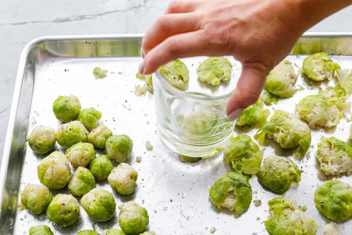 Angle shot of someone smashing boiled, oiled, and seasoned Brussels sprouts. 