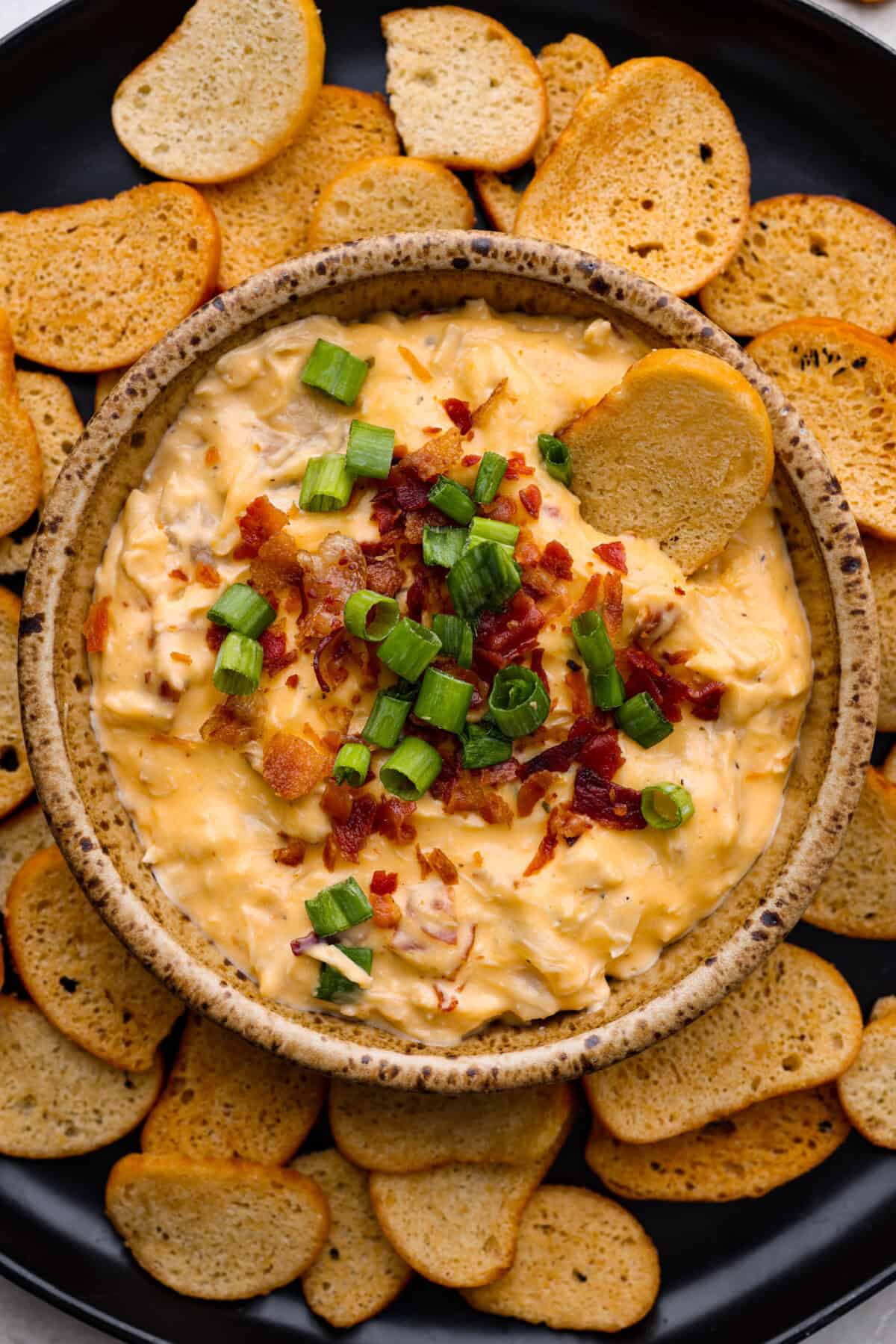 Overhead shot of slow cooker crack chicken dip in a bowl surrounded by toasted baguette pieces. 