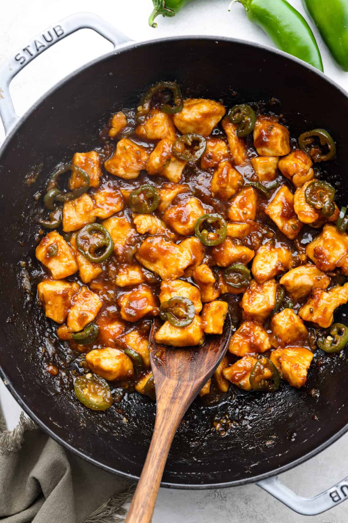 Close up shot of jalapeño chicken with a wooden serving spoon in a skillet. 