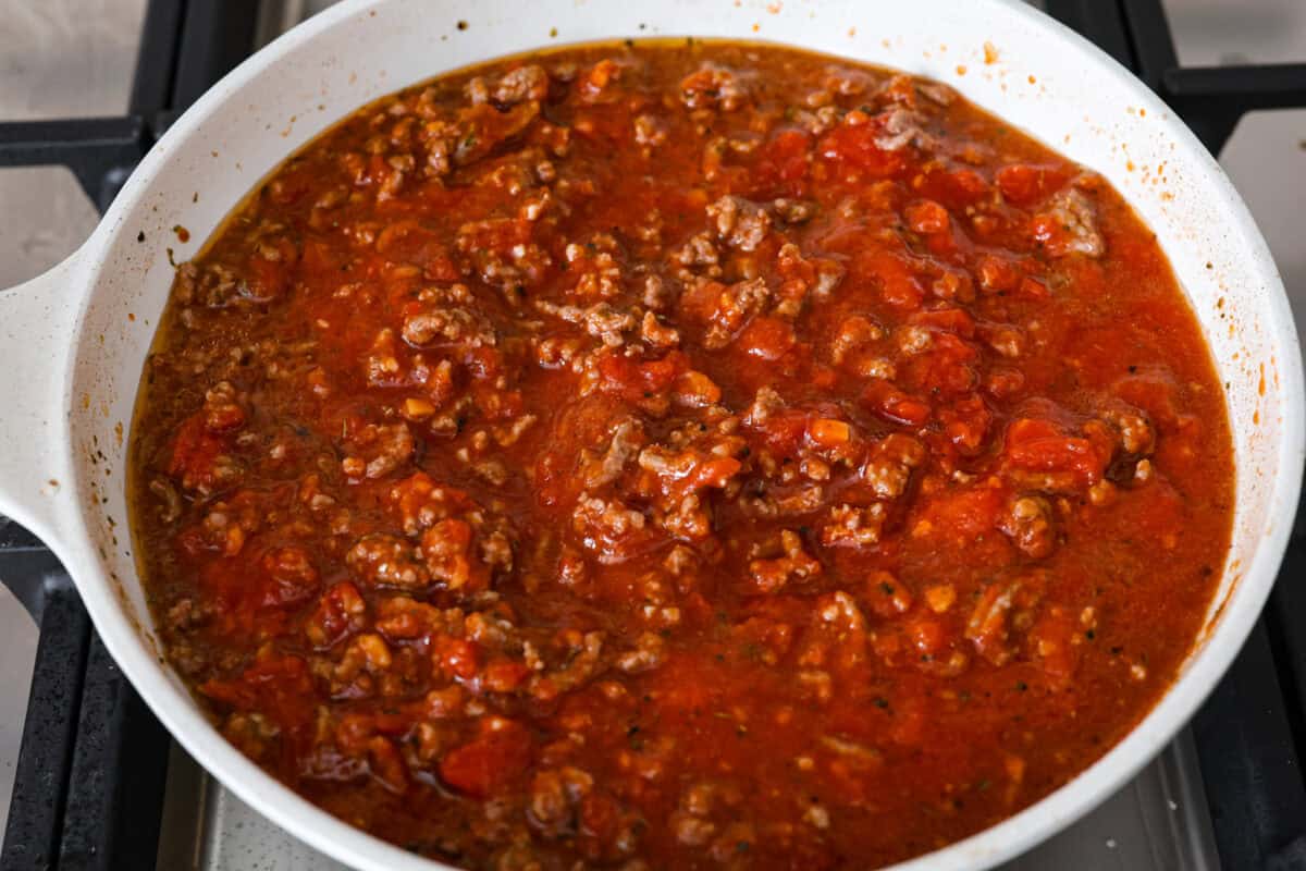 Overhead shot of browned meat and seasonings with marinara sauce poured over the top in a skillet. 