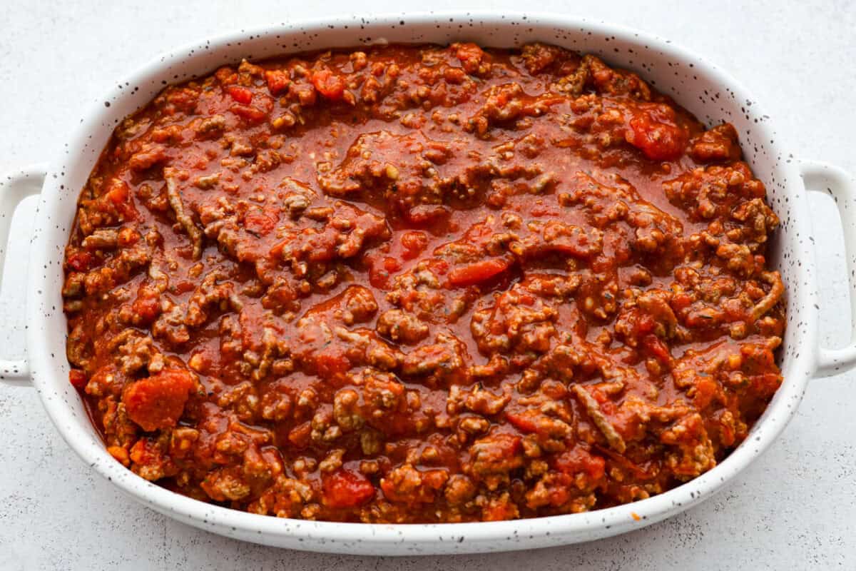 Overhead shot of meat and marinara poured over the top of the ravioli and cheese in the baking dish.