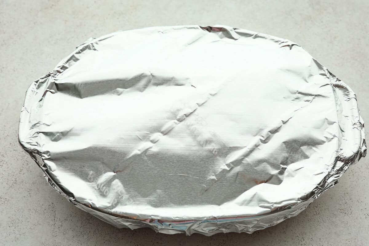 Million Dollar Ravioli Casserole is a flavorful casserole version of the classic! It's easy to make with mouthwatering layers of cheesy ravioli, meat sauce, and melted mozzarella cheese on top. This is a comforting, family-friendly dinner that you'll be craving on repeat! Overhead shot of million dollar ravioli casserole ready to be baked with aluminum foil over the top.
