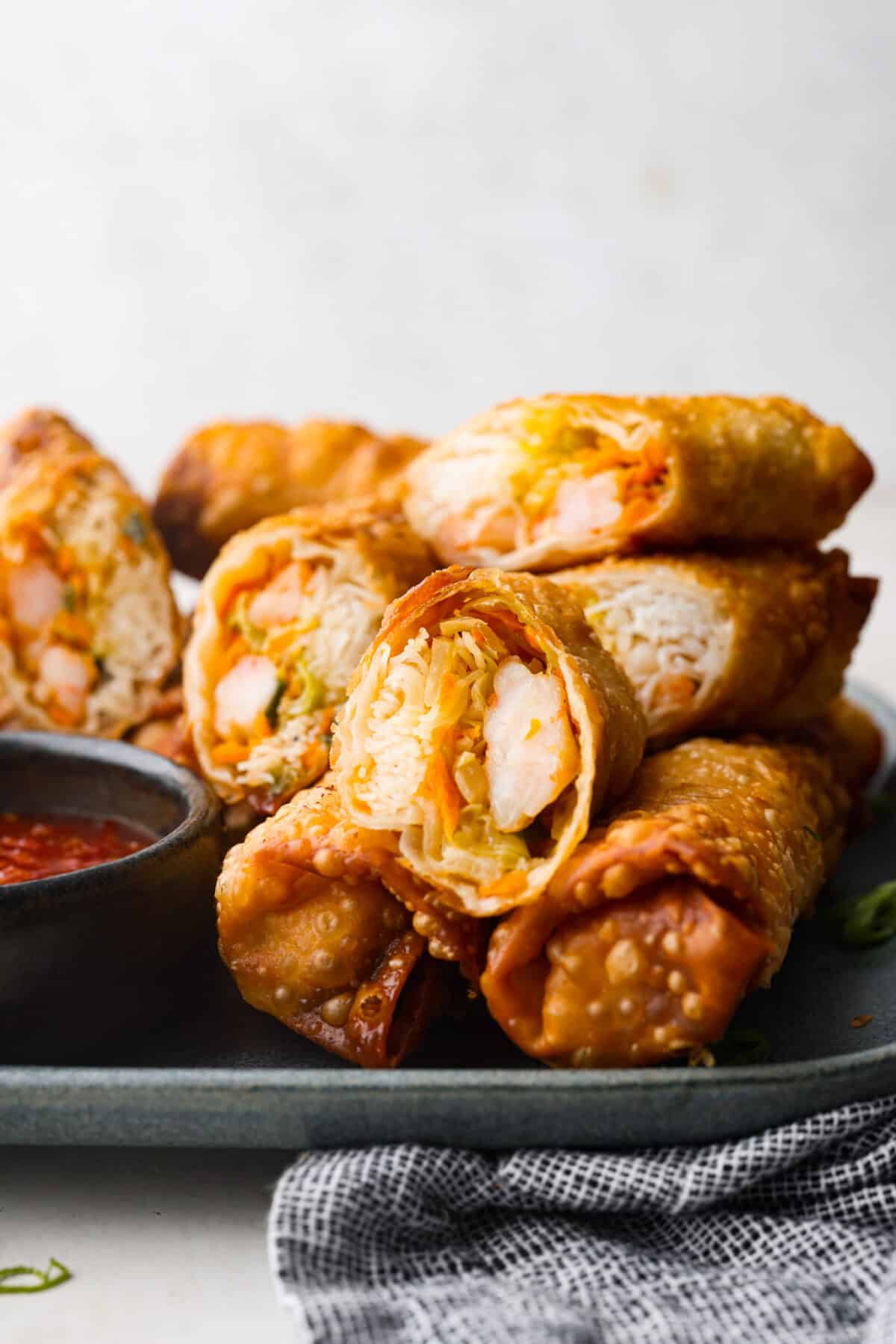 Side shot of egg rolls stacked on a plate with some of the rolls cut in half. 