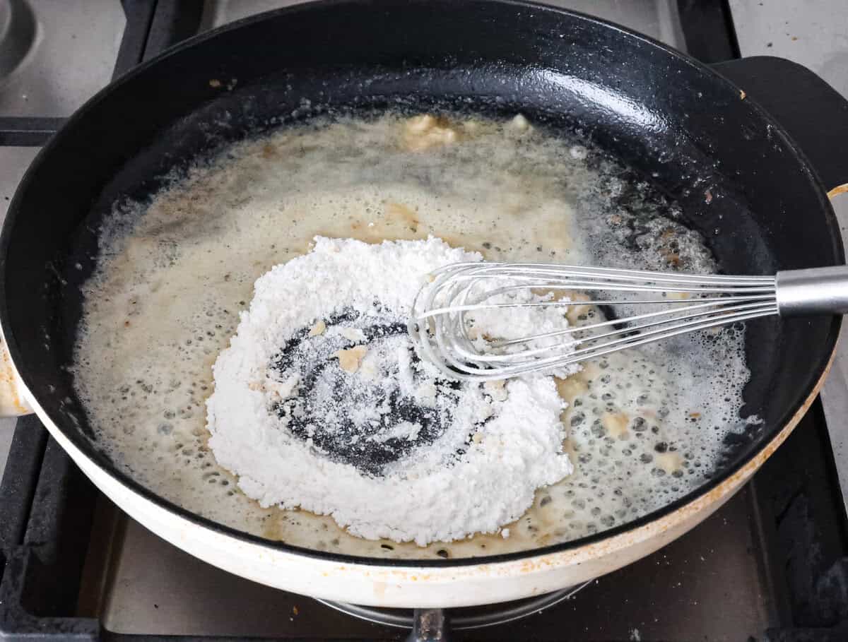 Smothered chicken is a flavorful comfort food full of rich, creamy gravy, tender chicken cutlets, and savory mushrooms. Perfect on its own or paired with mashed potatoes, rice or pasta, you're family will definitely want this on the weekly meal plan. Overhead shot of flour being whisked into butter at the bottom of skillet.