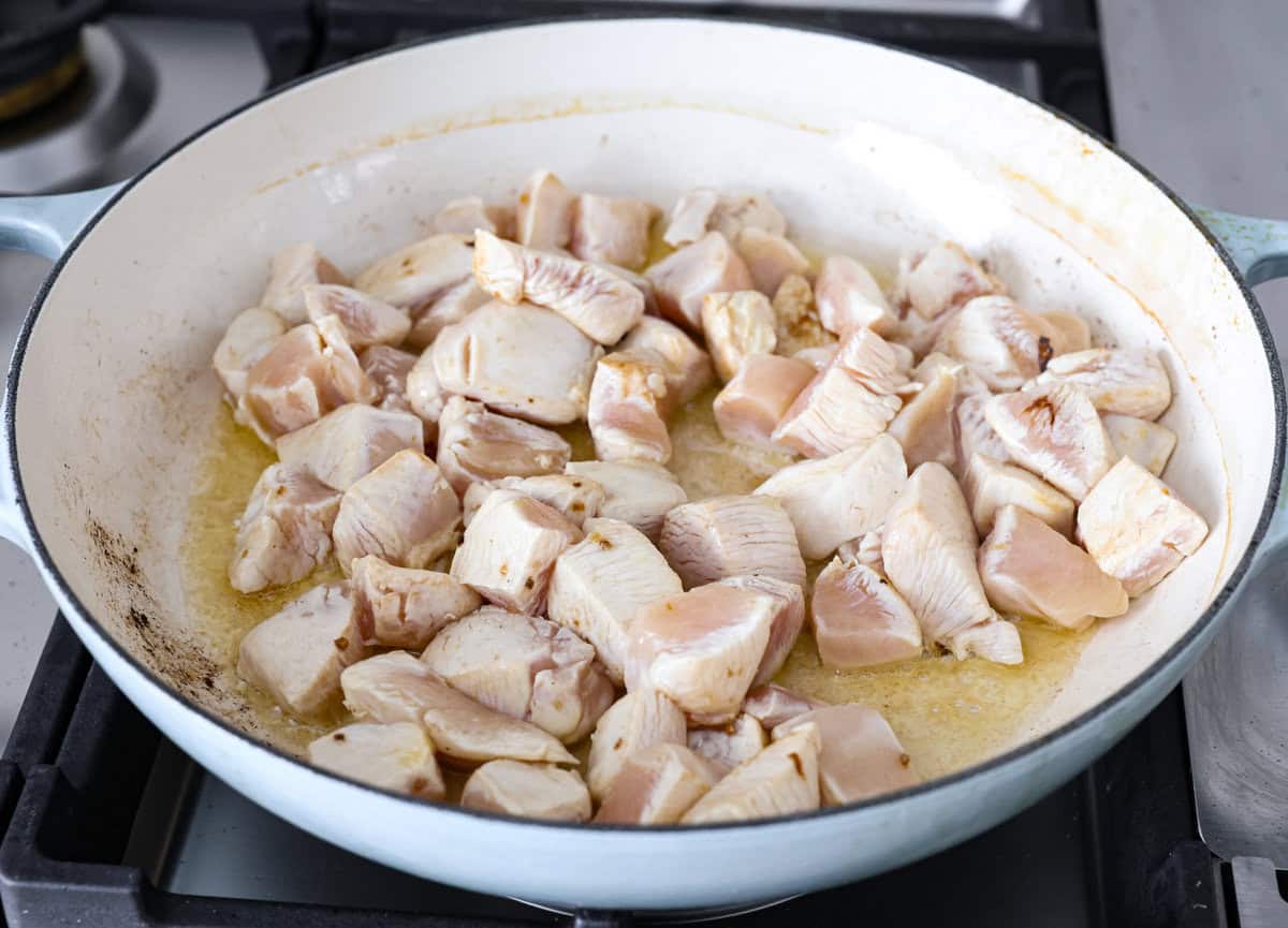 Chicken korma is a traditional Indian chicken dish. It's made with tender chicken smothered in a creamy, wonderfully seasoned sauce. It's so good your family will think you got takeout! Angle shot of chicken being searing in oil and ghee in a skillet.