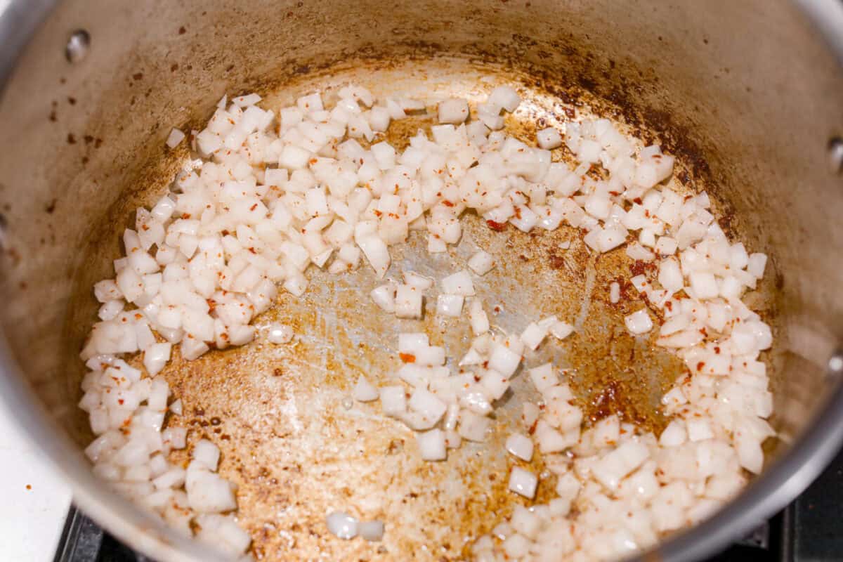 Overhead shot of onions being cooked in the pot with the bacon and sausage drippings. 