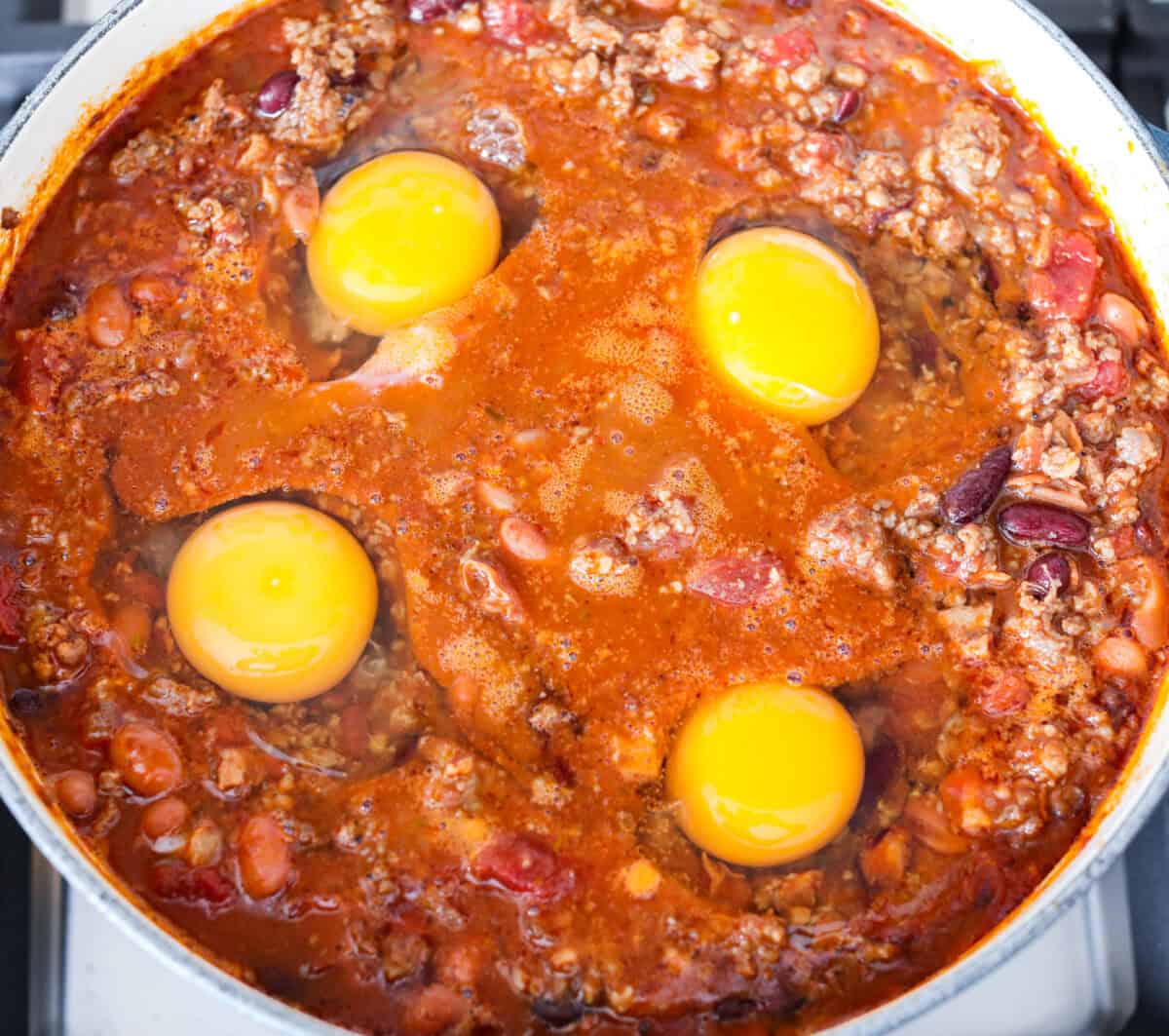 Overhead shot of chili with 4 raw eggs over the top. 