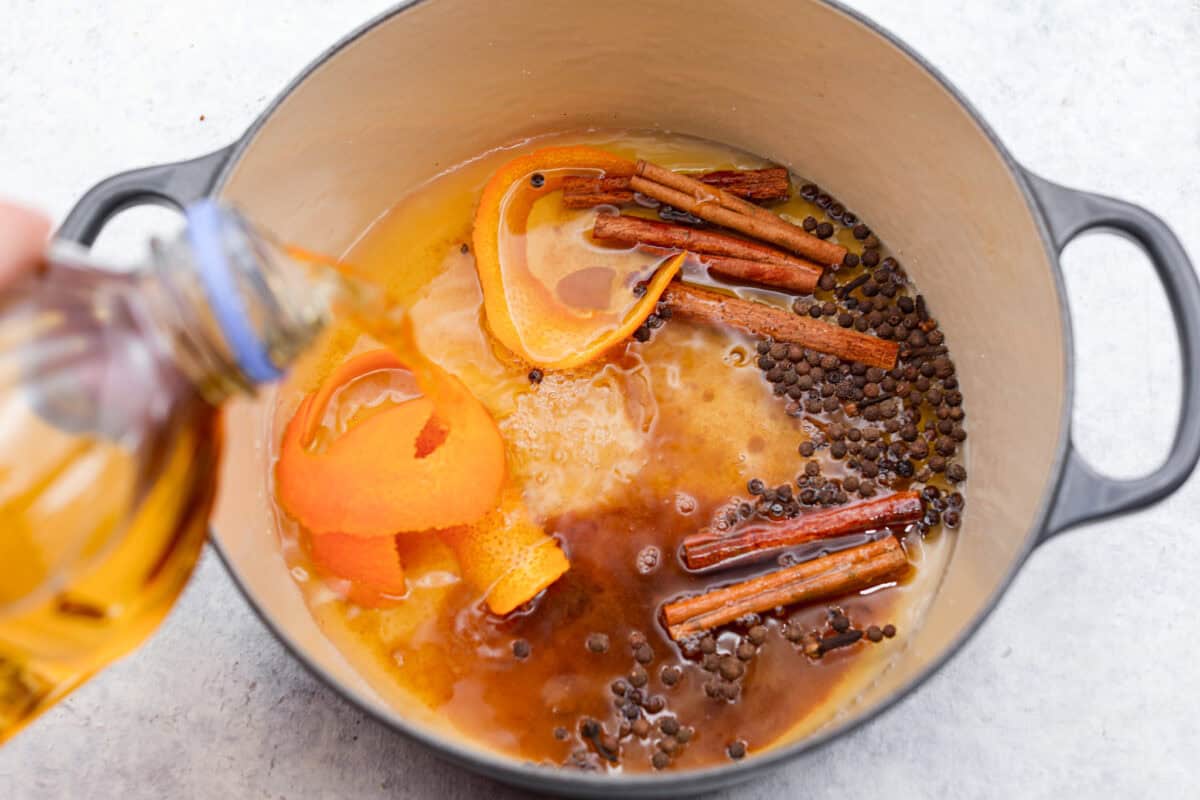 Overhead shot of ingredients in the pot while someone pours apple cider over the top. 