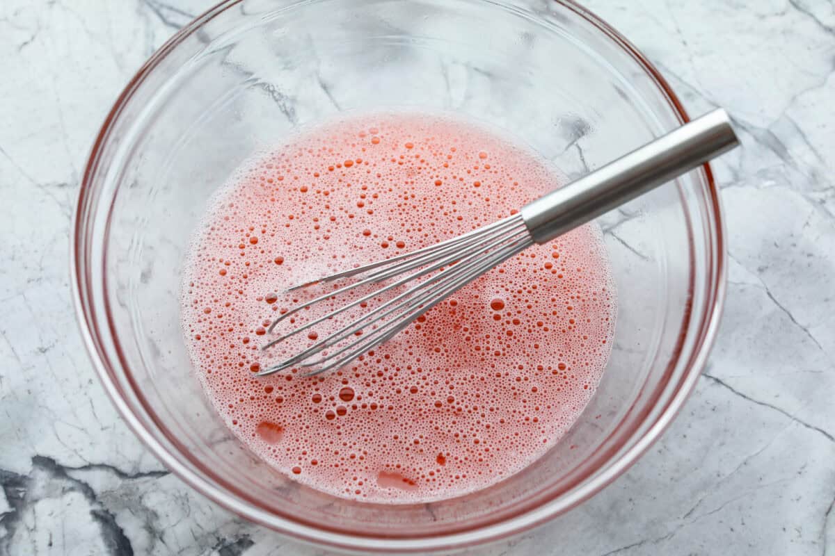 Jello and water in a glass bowl with a whisk. 