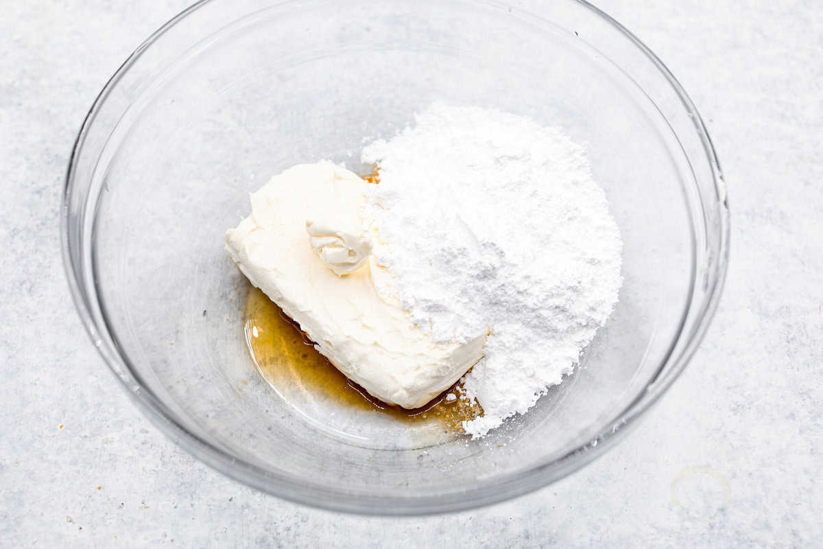Fall in love with this Pumpkin Delight! A shortbread crust topped with a fluffy cheesecake mixture, a creamy pumpkin layer, and whipped topping. Every bite of this irresistible layered dessert is pumpkin heaven! Third photo of the cheesecake layer ingredients in a bowl.