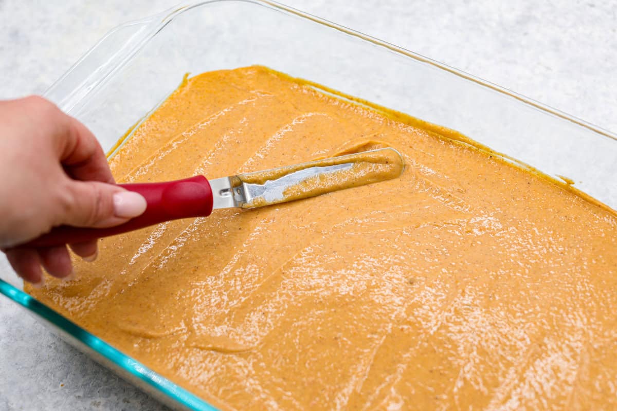 Fall in love with this Pumpkin Delight! A shortbread crust topped with a fluffy cheesecake mixture, a creamy pumpkin layer, and whipped topping. Every bite of this irresistible layered dessert is pumpkin heaven! Sixth photo of the pumpkin layer spreading on the cheesecake layer.