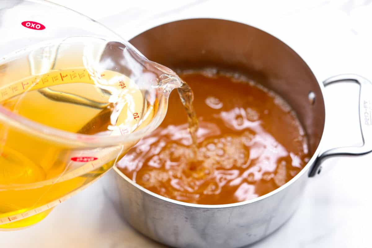 Overhead shot of someone pouring apple juice into the pan filled with strained juice. 