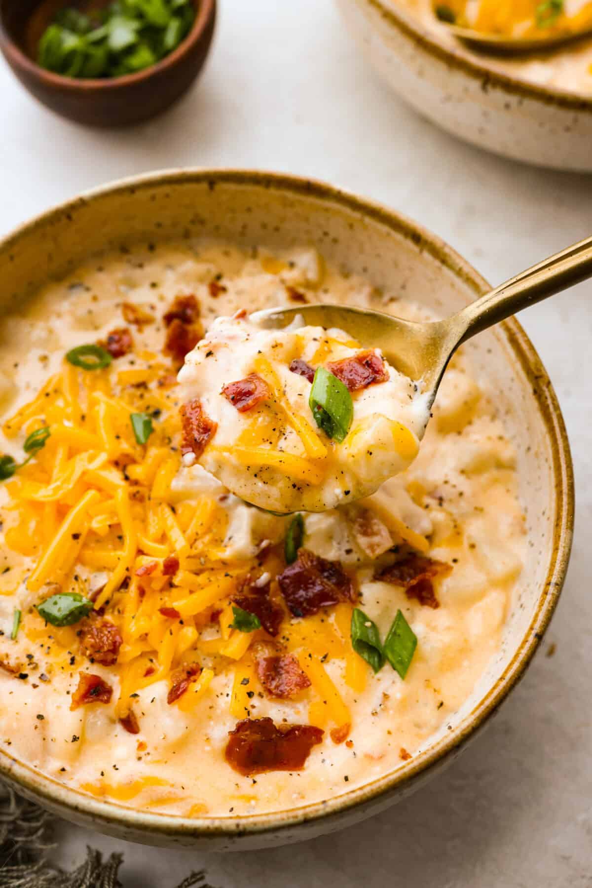 Close up photo of crock pot cracked potato soup on a spoon over a bowl. 