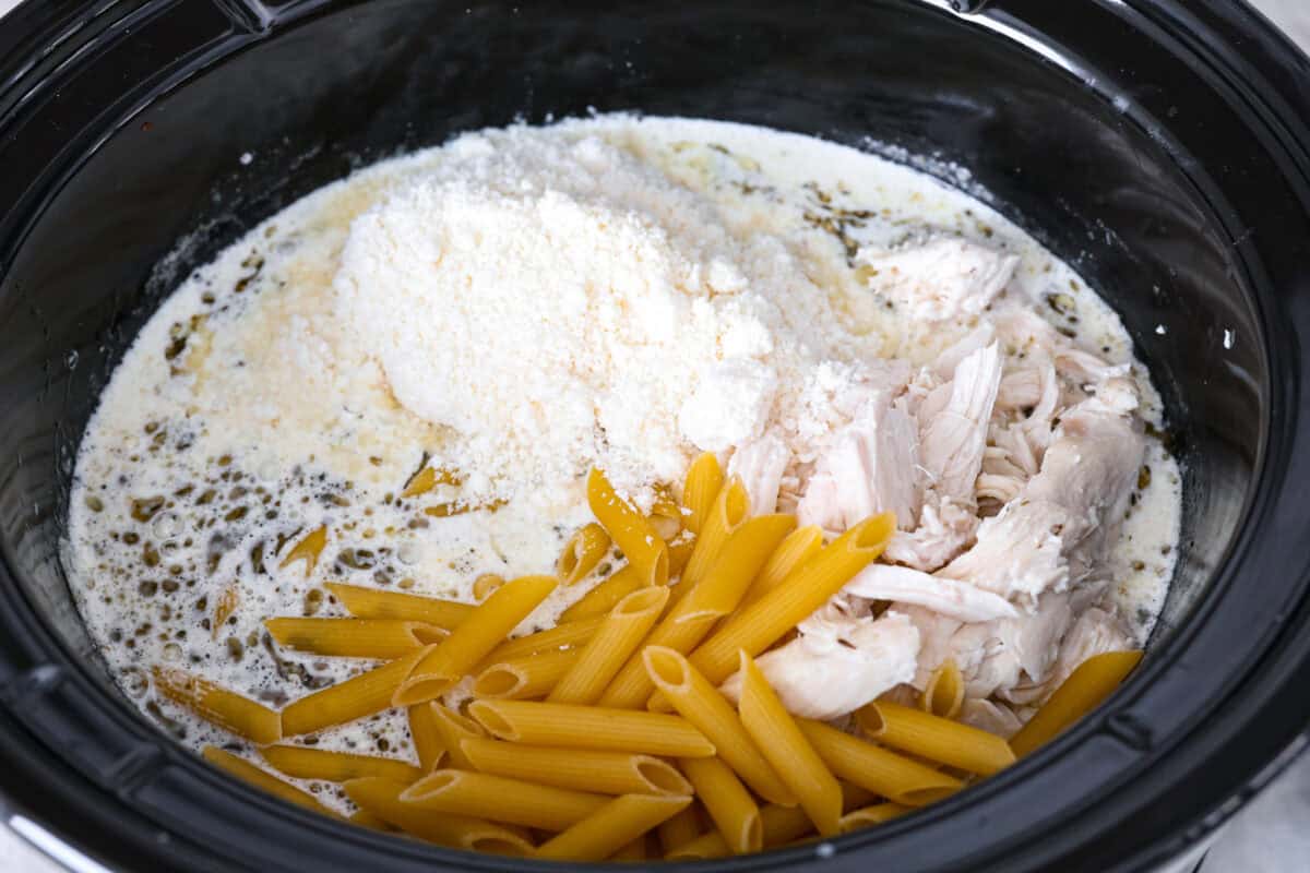 Overhead shot of pasta, chicken and parmesan cheese added back into the crockpot. 