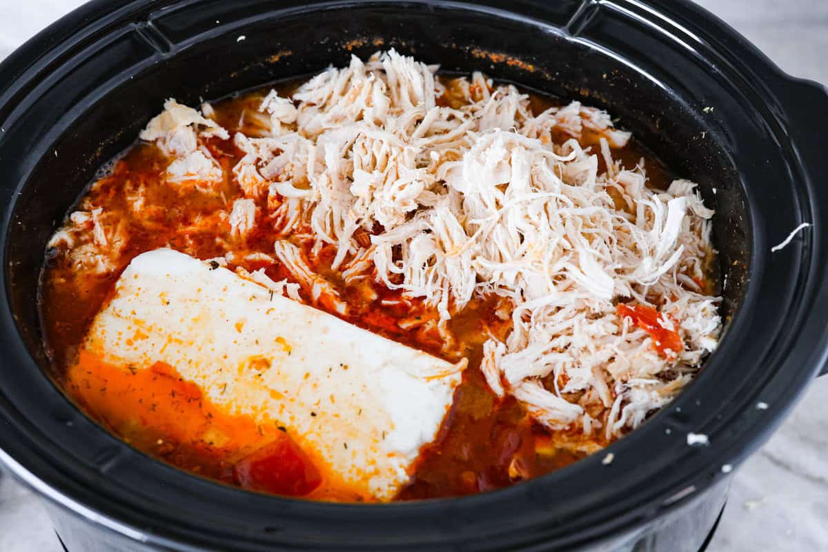 Crockpot buffalo chicken chili is a buffalo wing lover's dream. It has a tangy, fiery buffalo hot sauce base mixed with shredded chicken, smooth cream cheese, tender beans, and vegetables. If you love buffalo wings, you will love this chili! Overhead shot of shredded chicken and cream cheese added back to the crockpot.