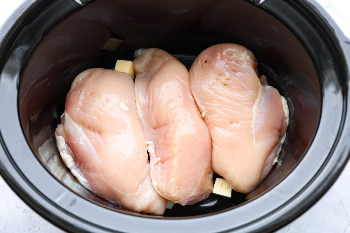 Overhead shot of chicken breasts and butter in the bottom of the crockpot. 