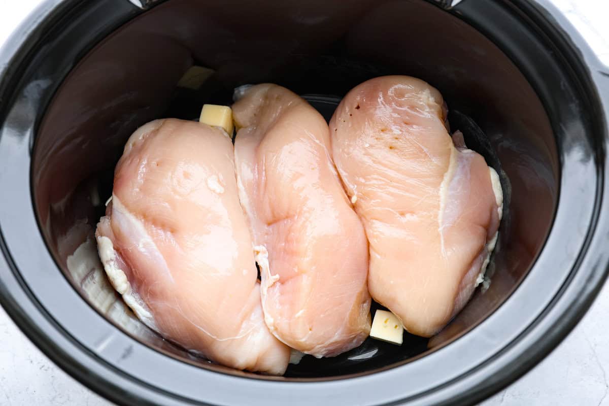 Crockpot buffalo chicken chili is a buffalo wing lover's dream. It has a tangy, fiery buffalo hot sauce base mixed with shredded chicken, smooth cream cheese, tender beans, and vegetables. If you love buffalo wings, you will love this chili! Overhead shot of chicken breasts and butter in the bottom of the crockpot.