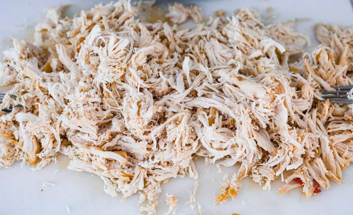 Crockpot buffalo chicken chili is a buffalo wing lover's dream. It has a tangy, fiery buffalo hot sauce base mixed with shredded chicken, smooth cream cheese, tender beans, and vegetables. If you love buffalo wings, you will love this chili! Angle shot of chicken shredded on a cutting board.