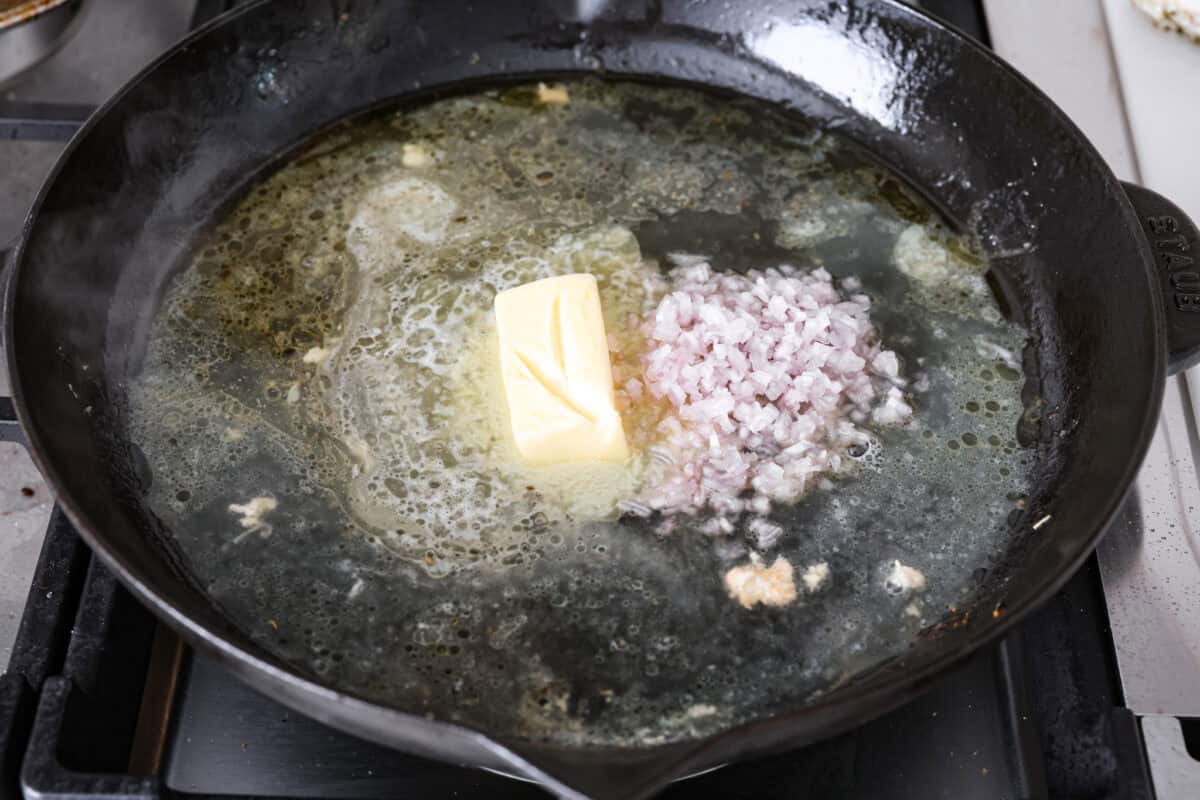 Angle shot of white wine, vinegar, chicken broth, butter and shallots in a skillet. 