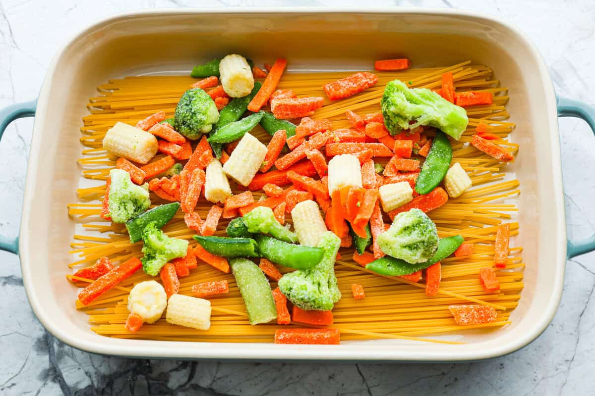 Honey Sesame Chicken Noodle Bake is the perfect dinner solution when you need something incredibly tasty and totally fuss-free! This is a complete meal with delicious Asian flavors in one pan, without needing to pre-cook anything. Overhead shot of frozen vegetables over noodles in a baking dish.