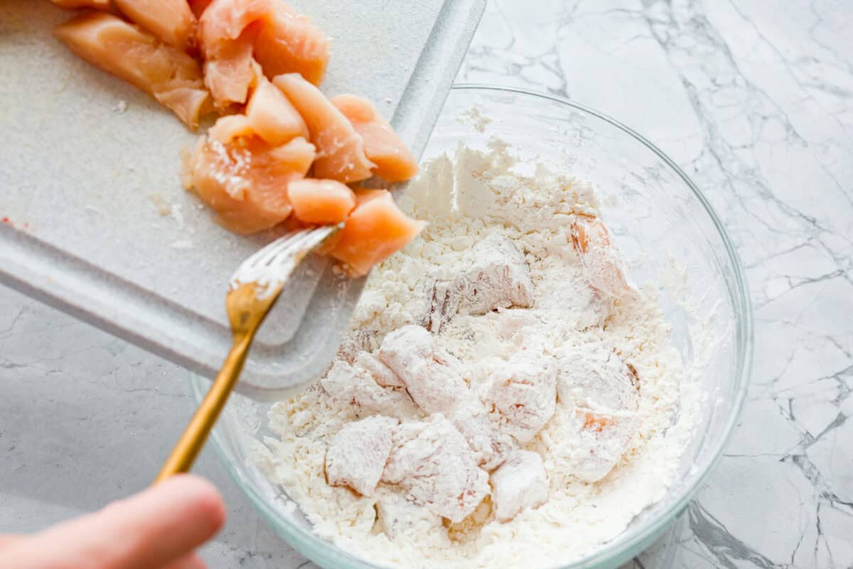 Overhead shot of cubed chicken being tossed in the flour mixture. 